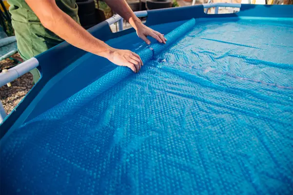 Person rollt eine blaue Poolabdeckung auf einem Aufstellpool aus