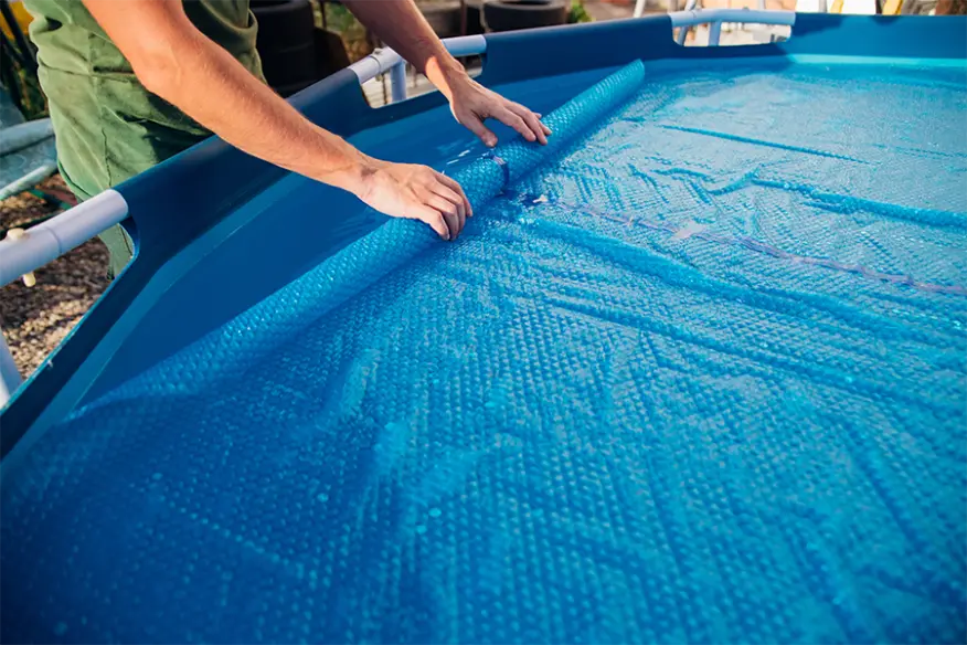 Person rollt eine blaue Poolabdeckung auf einem Aufstellpool aus